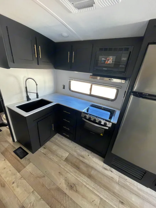 Sleek RV rental kitchen featuring black cabinets, white countertops, modern black appliances, and a full-size fridge.. Keystone RV Springdale 2023