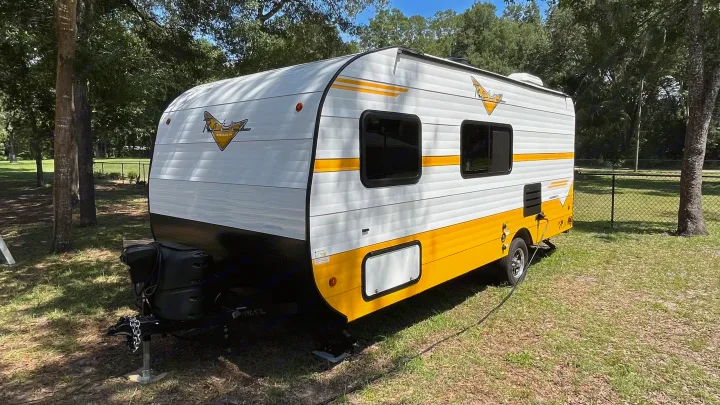 Bright white and yellow travel trailer RV rental parked on a grassy campsite.. Riverside RV Retro 2022