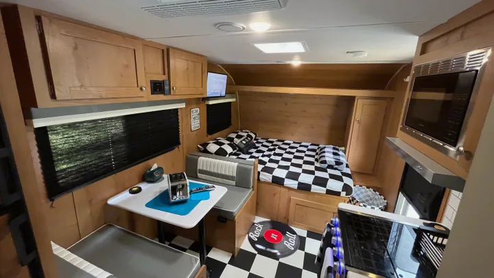 Retro-themed RV rental interior featuring a dinette, bed, and kitchen. Black and white checkered decor creates a fun vibe.. Riverside RV Retro 2022