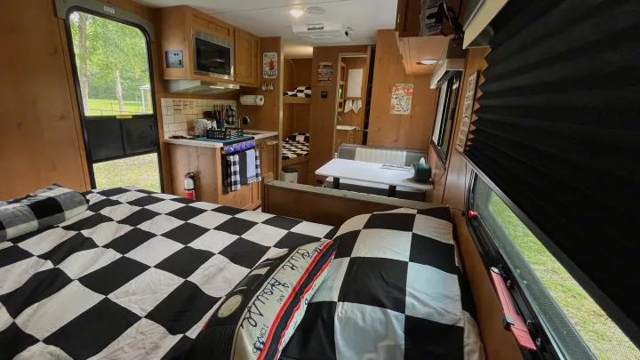 Interior of a retro-themed RV rental with black and white checkered bedding, a compact kitchen, and a dining booth, leading to bunk beds.. Riverside RV Retro 2022