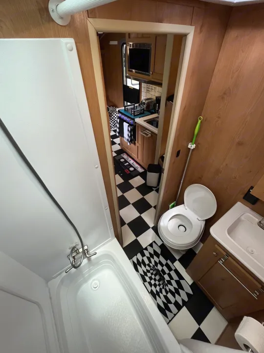 RV rental interior: practical bathroom with shower, toilet, sink & checkered kitchen. Perfect camper living space.. Riverside RV Retro 2022