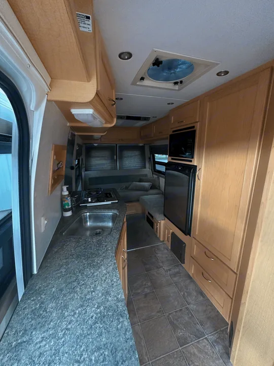 Efficient RV rental interior showcasing a compact kitchen with sink, stove, microwave, fridge, and comfortable living space.. Pleasure-Way Pleasure-Way Class B 2005
