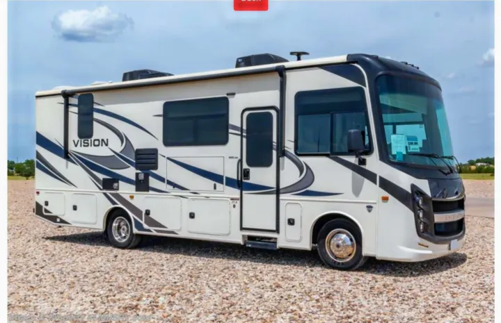 A white and black Class A motorhome, ideal for an RV rental, sits on a gravel lot under a blue sky, featuring 'VISION' graphics.. Entegra Coach Vision 2021