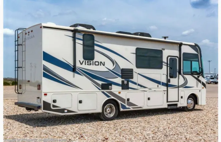 White 'Vision' RV rental motorhome with blue/gray graphics, parked on a gravel lot. Ideal for road trip adventures and comfortable travel.. Entegra Coach Vision 2021