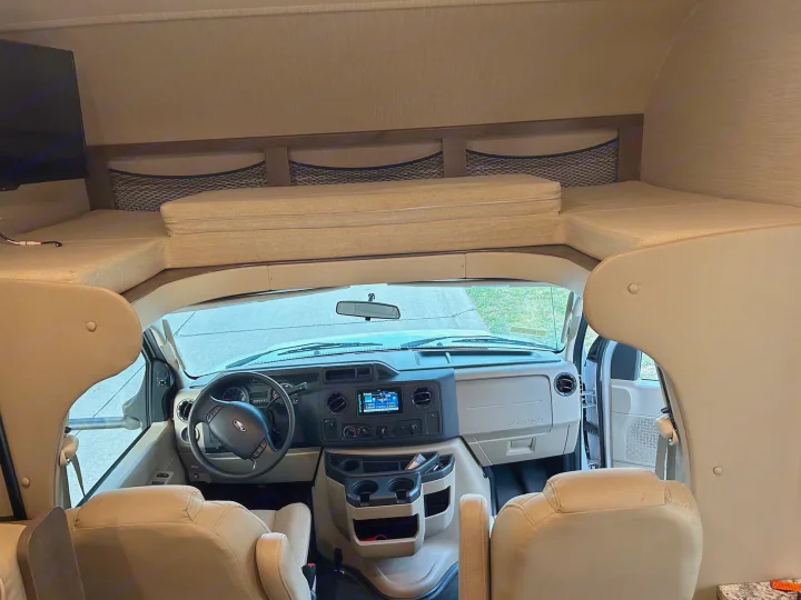 View of an rv rental's spacious interior, highlighting the driver's area and integrated bunk bed for extra sleeping.. Jayco Redhawk 2020