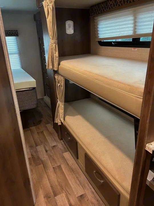 RV rental interior: bunk beds with curtains, lower storage drawers, and a separate windowed sleeping area with a wood floor.. Jayco Redhawk 2020