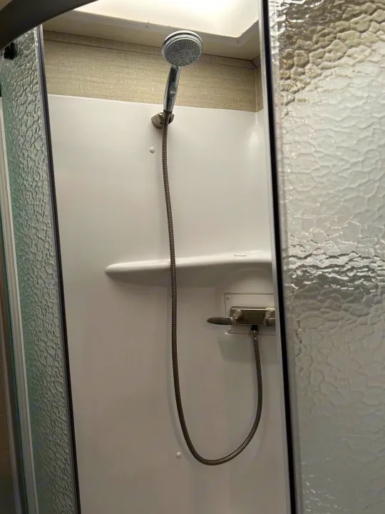 Clean and compact RV rental shower with handheld showerhead, integrated shelf, and water controls, ideal for travel.. Jayco Redhawk 2020