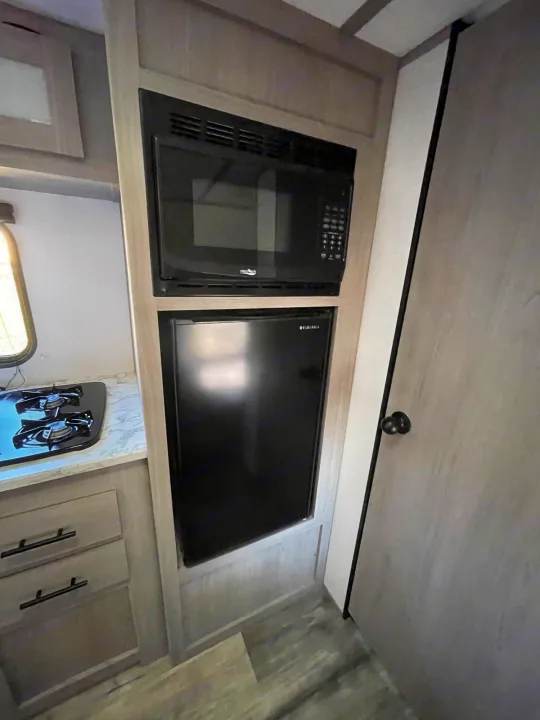 Explore this RV rental's modern kitchen: black microwave, Insignia fridge, two-burner stove, and sleek light cabinets.. Coleman Coleman Lantern 17B 2023