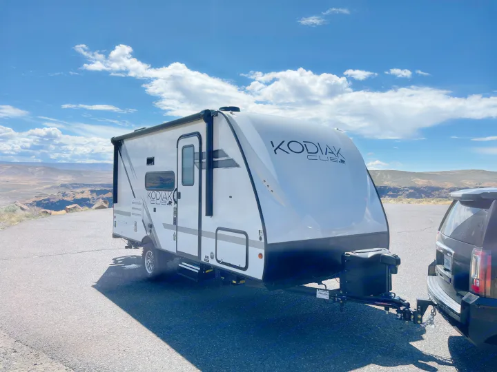 RV rental: A Kodiak Cub travel trailer hitched to an SUV, parked at a sunny scenic overlook with a vast landscape.. Dutchmen Kodiak Cub 175BH 2022