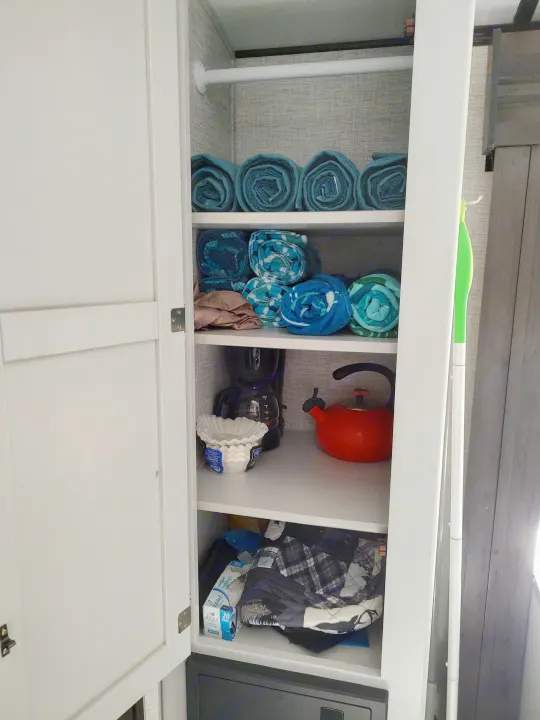 RV rental storage showcases neatly rolled towels, kitchenware (kettle, coffee filters), and linens, maximizing space for travelers.. Keystone RV Bullet Ultra Lite 2021