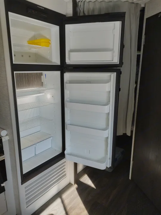RV rental interior: Open Dometic fridge/freezer showing empty compartments and shelves, ready for use.. Keystone RV Bullet Ultra Lite 2021