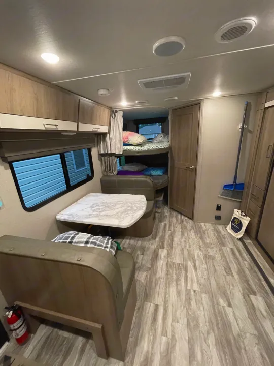 RV rental interior features a dinette, bunk beds, and wood-look flooring. Overhead cabinets & bright lighting enhance the space.. Grand Design Imagine XLS 2022