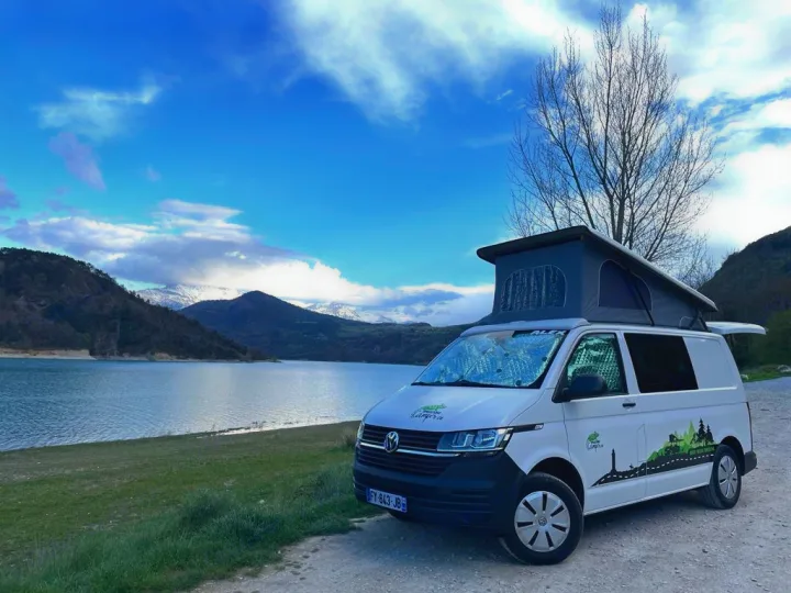 White camper van (RV rental) by a clear lake with snowy mountains & blue sky. Ideal for outdoor adventures.. Volkswagen Transporter T6.1 2021
