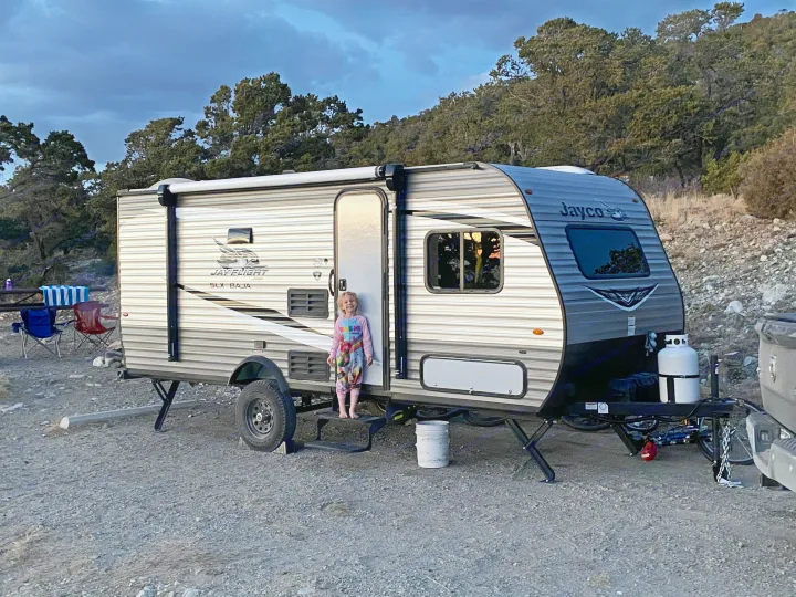 A child smiles barefoot on the steps of a Jayco travel trailer, showing the joy of an RV rental family camping trip.. Jayco Jay Flight SLX Baja Edition 2020