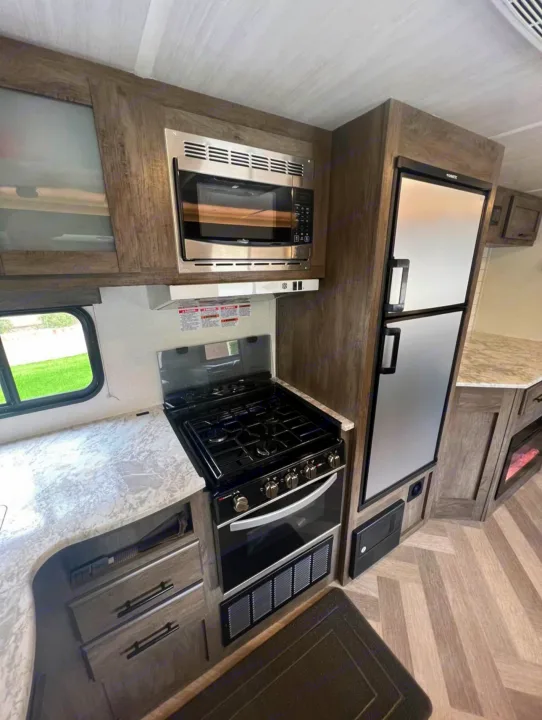 Spacious, modern RV rental kitchen with microwave, gas stove, oven, refrigerator, and stylish wood-look cabinets.. Forest River Wildwood 2021