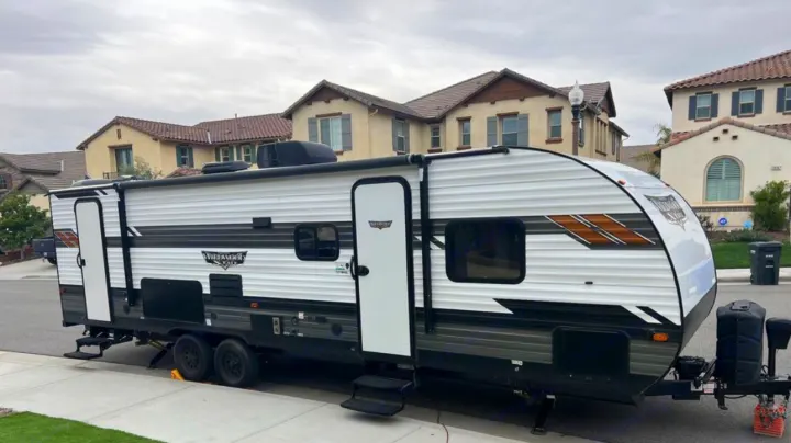 A white and black travel trailer RV, ideal for an rv rental getaway, parked on a quiet residential street.. Forest River Wildwood 2021