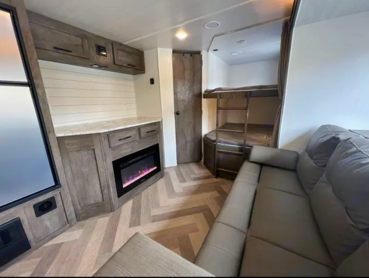 Inside this RV rental: a cozy grey sofa, built-in bunk beds, electric fireplace, and ample storage cabinetry.. Forest River Wildwood 2021