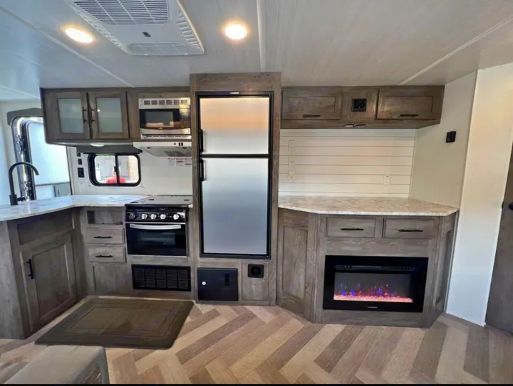Modern RV rental kitchen and living space with microwave, stove, fridge, and electric fireplace.. Forest River Wildwood 2021