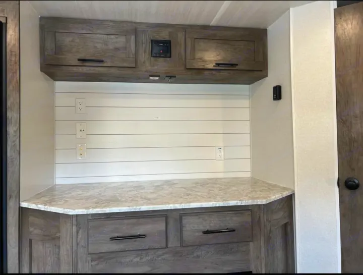 RV rental's modern interior: wood-grain cabinets, white shiplap wall, and marbled countertop. Features multiple outlets.. Forest River Wildwood 2021