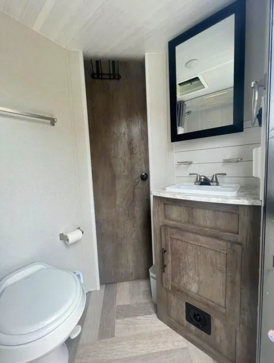 Clean RV rental bathroom with toilet, sink vanity, and mirror, featuring a compact design suitable for travel.. Forest River Wildwood 2021