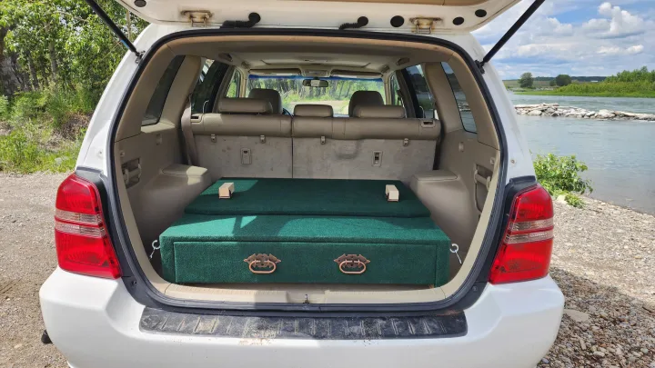 Green custom-built car camping bed inside SUV. Parked by a river, perfect for trips without an RV rental.. Toyota Highlander 2005