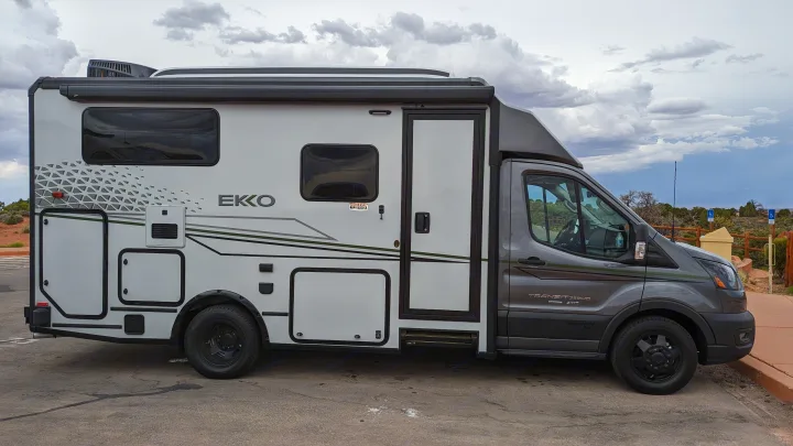A modern white and gray Winnebago Ekko rv rental parked on asphalt, set against a cloudy desert landscape. Perfect for adventures.. Winnebago Ekko 2023