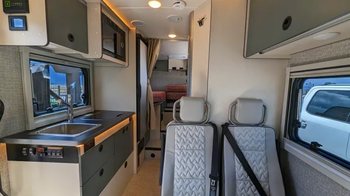 Inside an RV rental: full kitchenette, two comfortable passenger seats, and a cozy bed area in the back.. Winnebago Ekko 2023