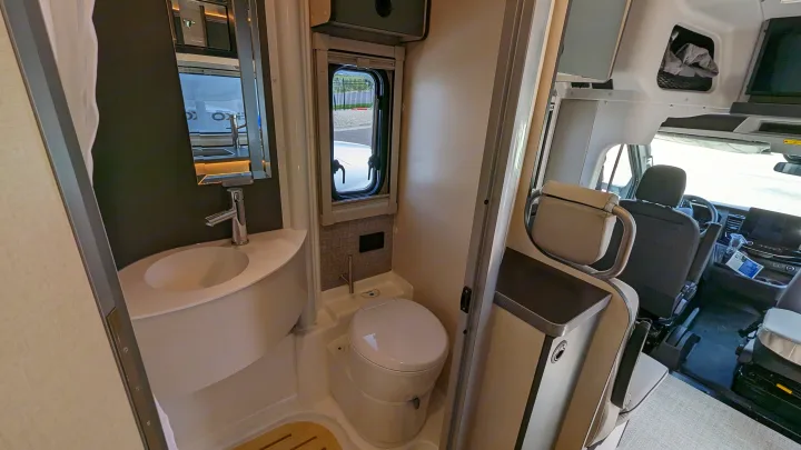 Compact bathroom with toilet and sink in an RV rental, plus a glimpse of the front cabin.. Winnebago Ekko 2023