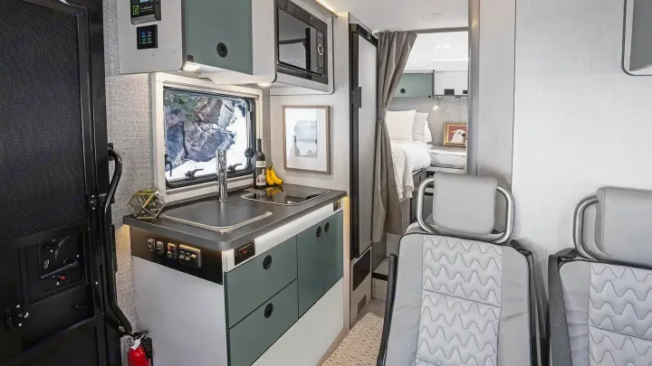 This modern RV rental interior features a compact kitchen, comfortable sleeping area, and front seats, ideal for mobile living.. Winnebago Ekko 2023