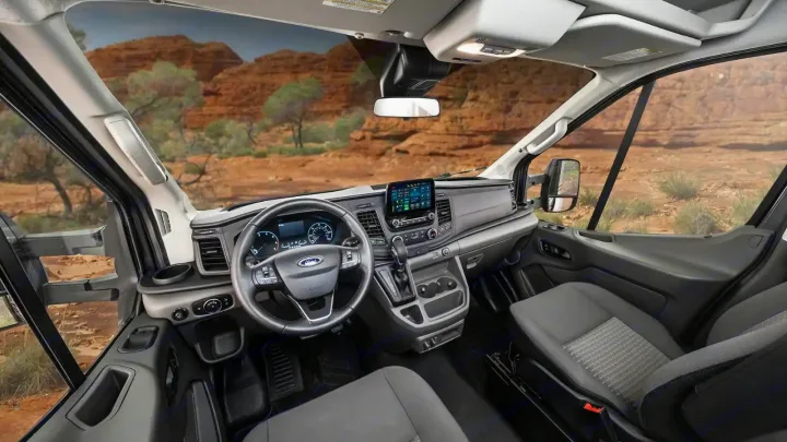 RV rental interior: Driver's perspective inside a modern van's cabin, showing dashboard, steering wheel, seats, and desert view.. Winnebago Ekko 2023