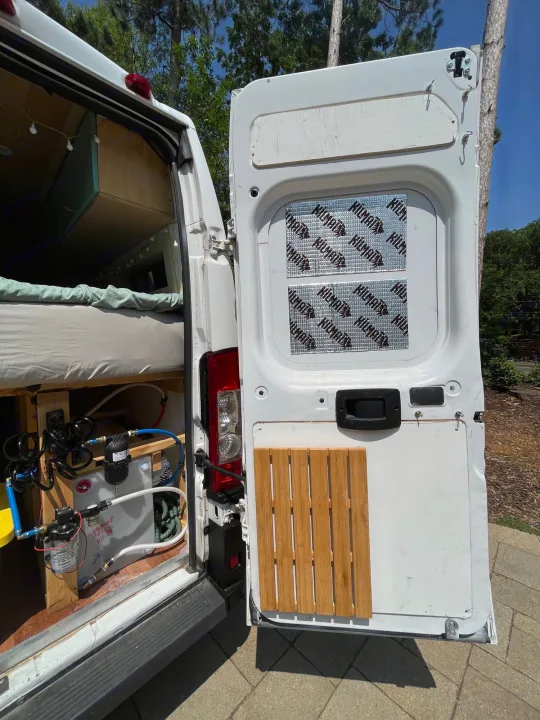 Open rear of an RV rental camper van shows a cozy bed, water system, and Kilmat sound-deadened door, ready for adventure.. Other Sprinter Van 2017