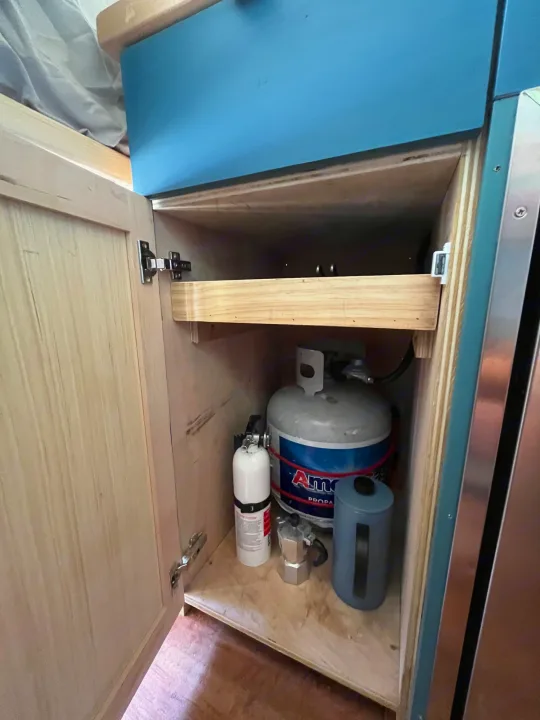 RV rental cabinet storage with propane tank, fire extinguisher, Moka pot, and pull-out shelf for compact living.. Other Sprinter Van 2017