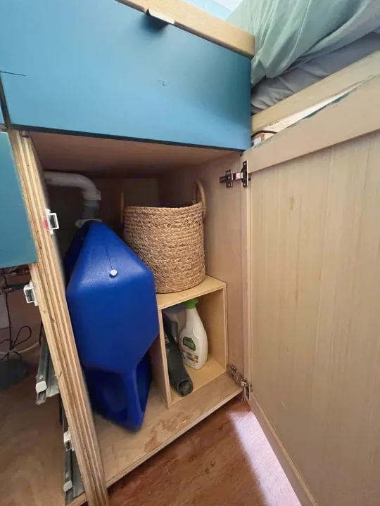 RV rental: Built-in storage unit with blue water tank, plumbing, woven basket, and cleaning supplies in a wooden cabinet.. Other Sprinter Van 2017