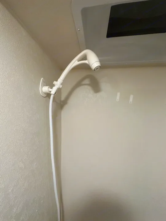 Compact RV rental shower featuring a white handheld showerhead and hose mounted to a wall.. Forest River Evo 2019