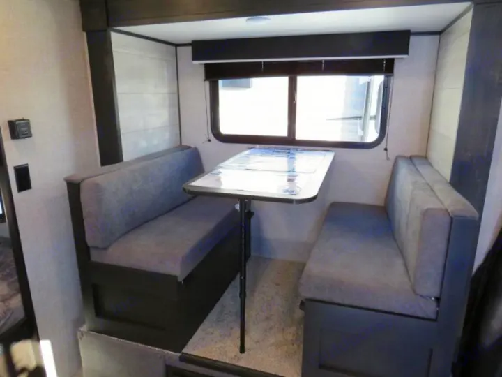 RV rental dinette: cozy gray benches & table by a window, ideal for meals or work on your next adventure.. Jayco Jay Flight SLX STX Edition 2023