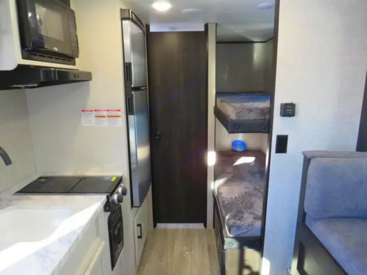 Interior of an RV rental featuring a compact kitchen, refrigerator, bunk beds, and seating area.. Jayco Jay Flight SLX STX Edition 2023