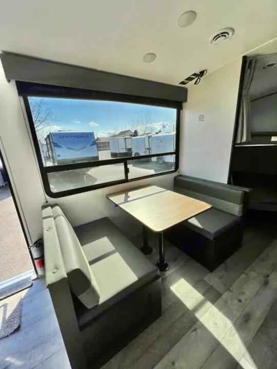RV rental dinette with cozy benches, a table, and a large window offering outdoor views, ideal for campers.. Keystone RV Springdale 2022