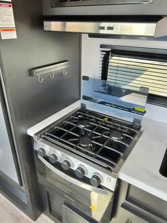 Modern RV rental kitchen showcasing a four-burner stove, oven, and sleek range hood for your on-the-go meals.. Keystone RV Springdale 2022