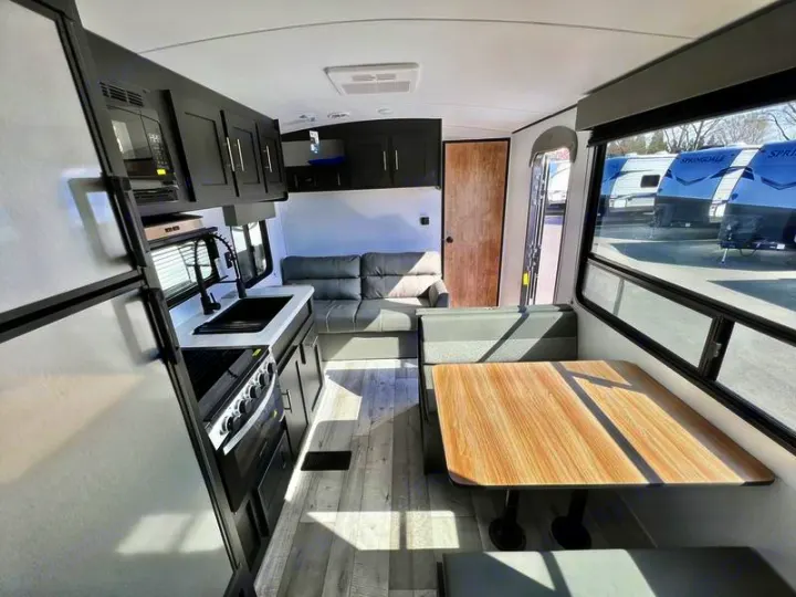 Kitchen with oven, dinette, & sofa define this RV rental. Large windows reveal other RVs outside.. Keystone RV Springdale 2022