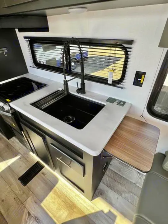 Inside this rv rental: a modern kitchen with black sink, stovetop, dark cabinets, and a clever pull-out counter.. Keystone RV Springdale 2022
