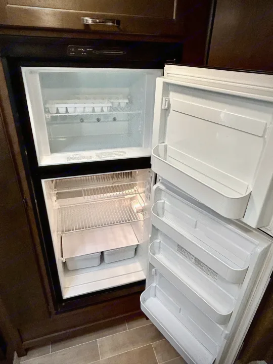 Open, very frosty RV refrigerator in an rv rental. Ice covers interior shelves, signaling a need for defrosting.. Thor Chateau 2020