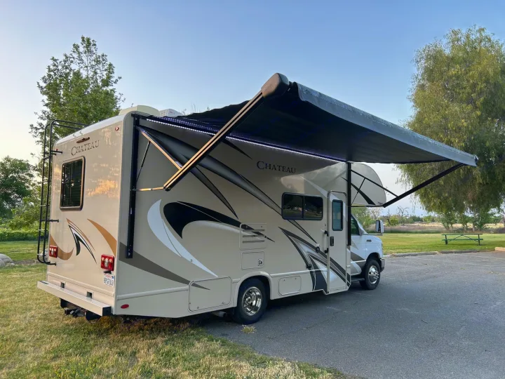 Chateau RV rental with extended, lit awning parked at a sunny campsite. Ideal for road trips and outdoor adventure.. Thor Chateau 2020