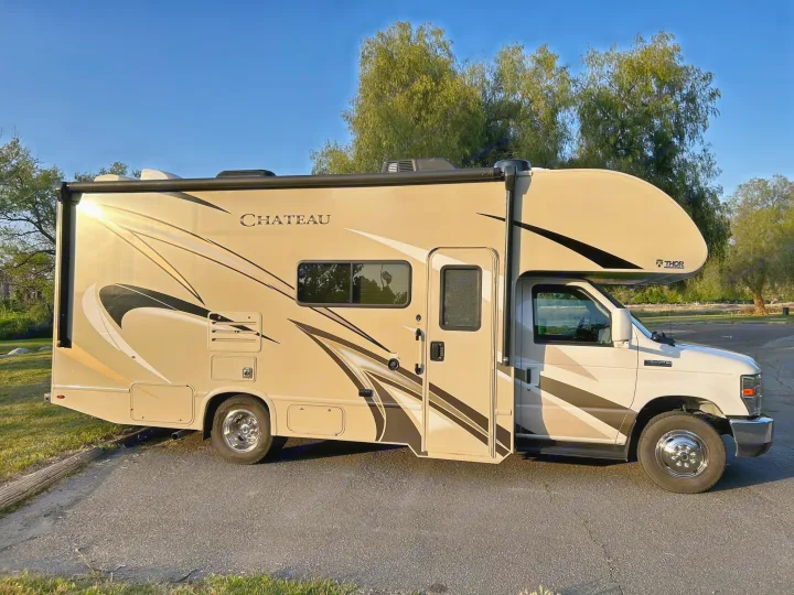 Side view of a tan and white Thor Chateau Class C RV rental, a recreational vehicle parked on asphalt outdoors.. Thor Chateau 2020