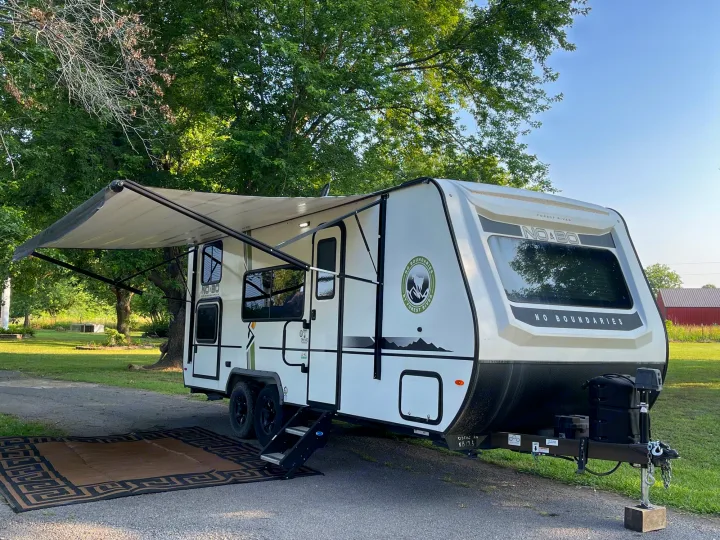 This white travel trailer RV rental is parked on gravel with its awning extended, ready for a comfortable outdoor stay.. Forest River No Boundary 2020