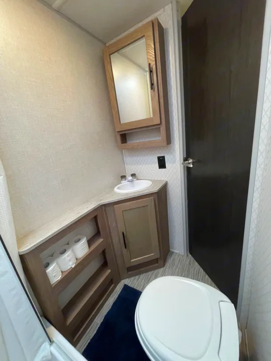 Compact RV rental bathroom with a sink, mirror cabinet, toilet, and integrated storage shelving visible.. Forest River No Boundary 2020