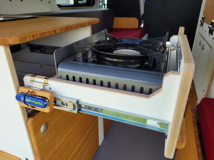 A handy pull-out gas stove integrated into an RV rental's mobile kitchen setup, with durable wooden cabinetry.. Opel VIVARO 2025