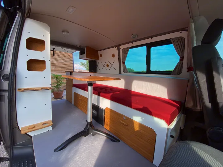 Step inside this cozy RV rental camper van! Features a red upholstered bed/bench, bamboo table, and sleek white/wood cabinetry.. Opel VIVARO 2025