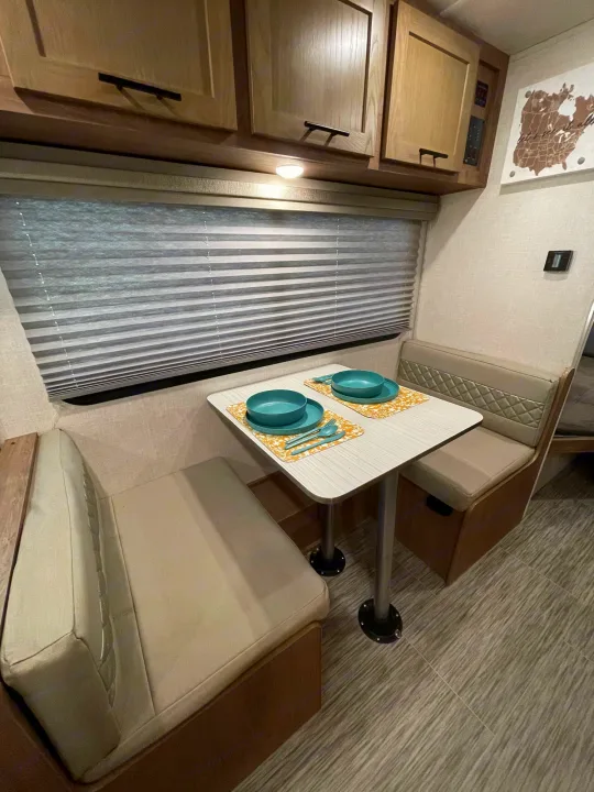 RV rental dinette: a light-toned interior with comfortable bench seating, a window, and a table set with teal dishes.. Forest River No Boundary 2020