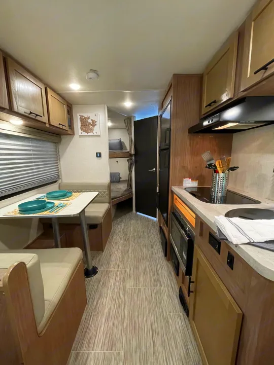 This compact RV rental interior features a well-equipped kitchenette, dining booth, and bunk beds, offering a functional living space.. Forest River No Boundary 2020