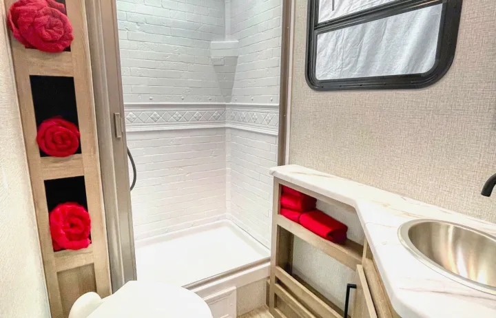 Clean RV rental bathroom with white shower, toilet, vanity, and bright red towels in cubbies. Ready for your travels.. Grand Design Other 2023